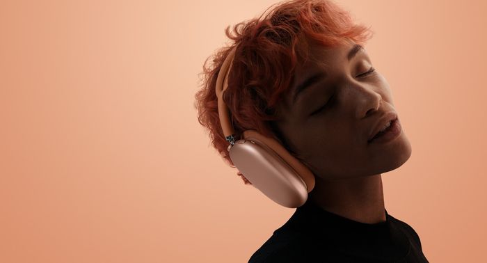 Apple AirPods Max - A person with head tilted and eyes closed wearing AirPods Max 2, orange color, over orange-pink background