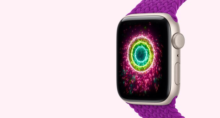 Apple Watch SE 3, starlight color aluminum case connected to magenta color Braided Solo Loop band, screen shows Activity rings styled as sparklers, pink, lime green, light blue concentric ri