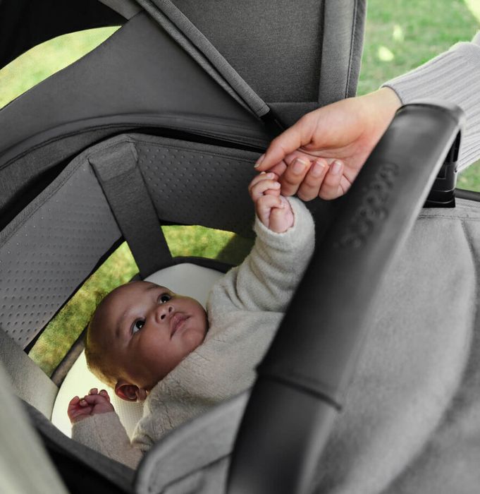 A newborn baby in the Bugaboo Fox 5 Renew bassinet reaches out to hold his parent's hand.
