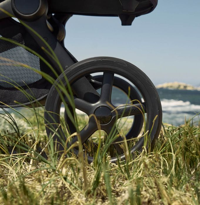 Close-up on the large wheels of the Bugaboo Fox 5 Renew all-terrain stroller as they roll on the grassy ground.