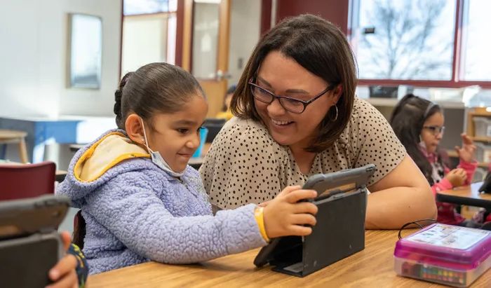 Smiling teacher helping a young student build english language skills with Khan Academy Kids.